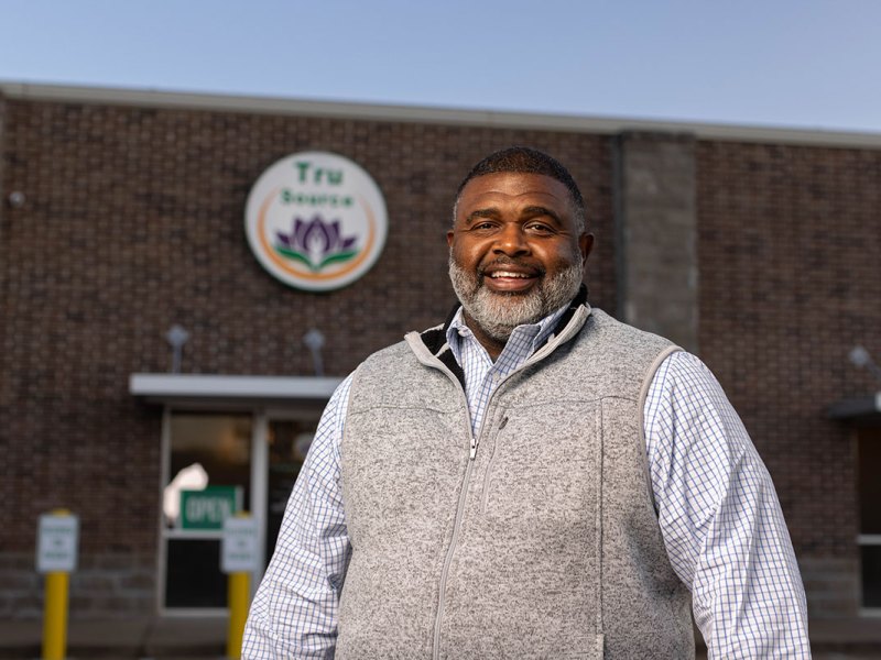 Clarence Cocroft stands outside of a business with a sign that reads Tru Source