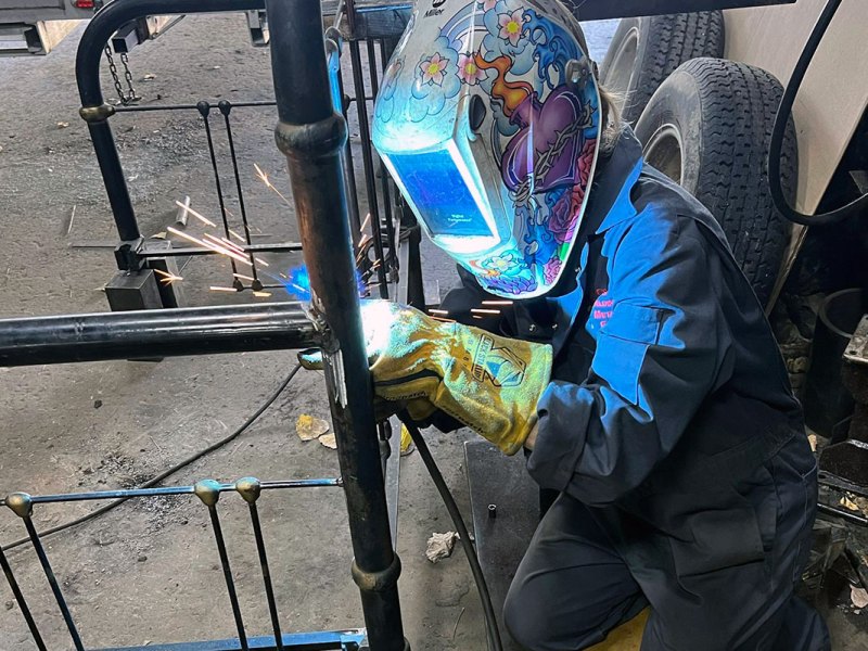 A person in a colorful helmet welds on a bedpost