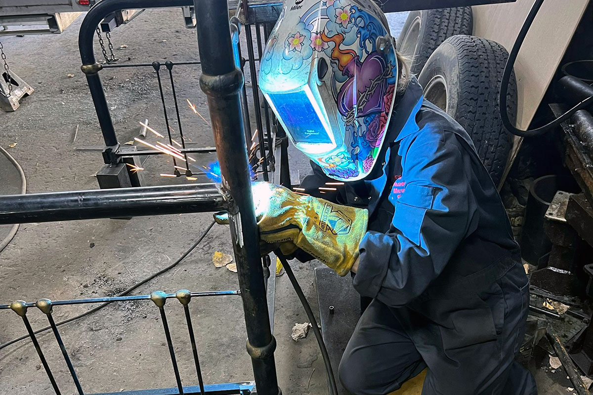 A person in a colorful helmet welds on a bedpost