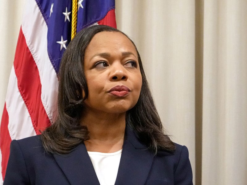 A woman stands in front of a US flag