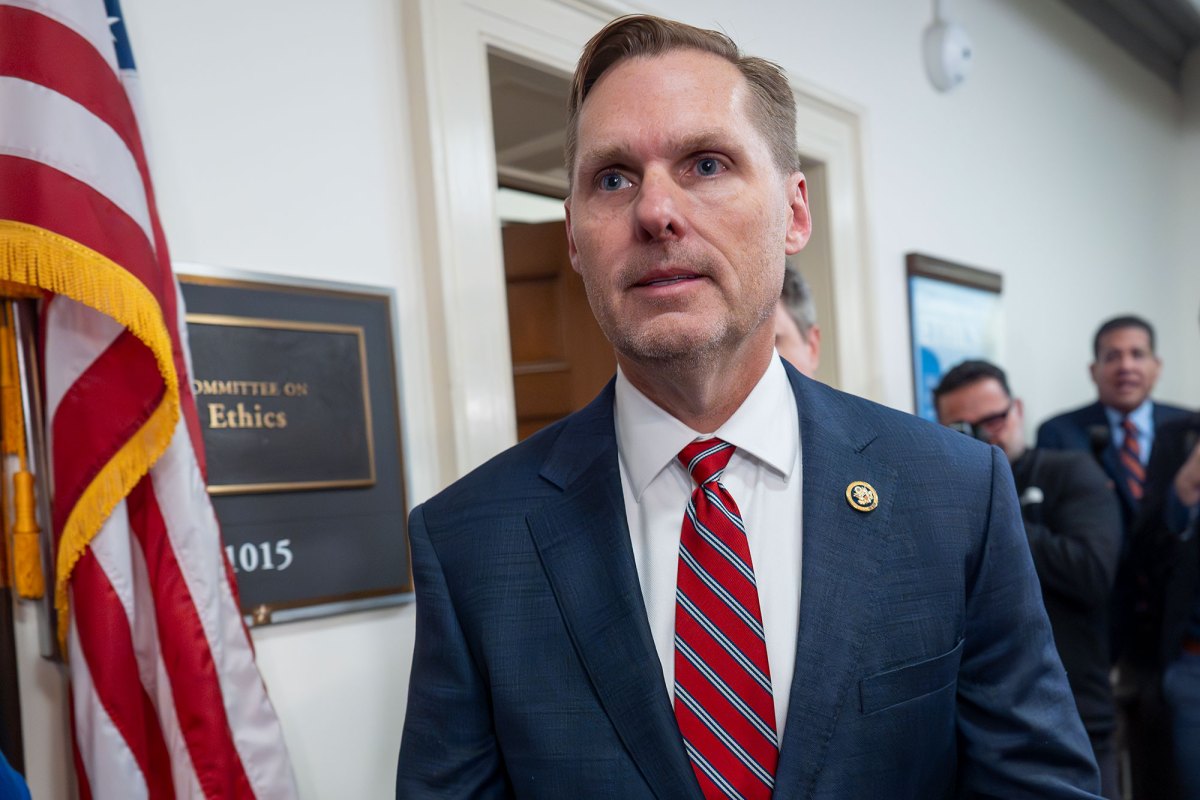 A man in suit and red tie walks past a doorway labeled Committee on Ethics
