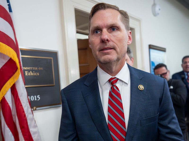 A man in suit and red tie walks past a doorway labeled Committee on Ethics