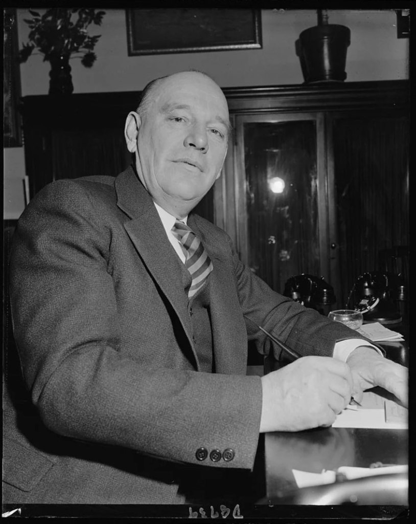Black and white photo of a man in a suit sitting at an office desk