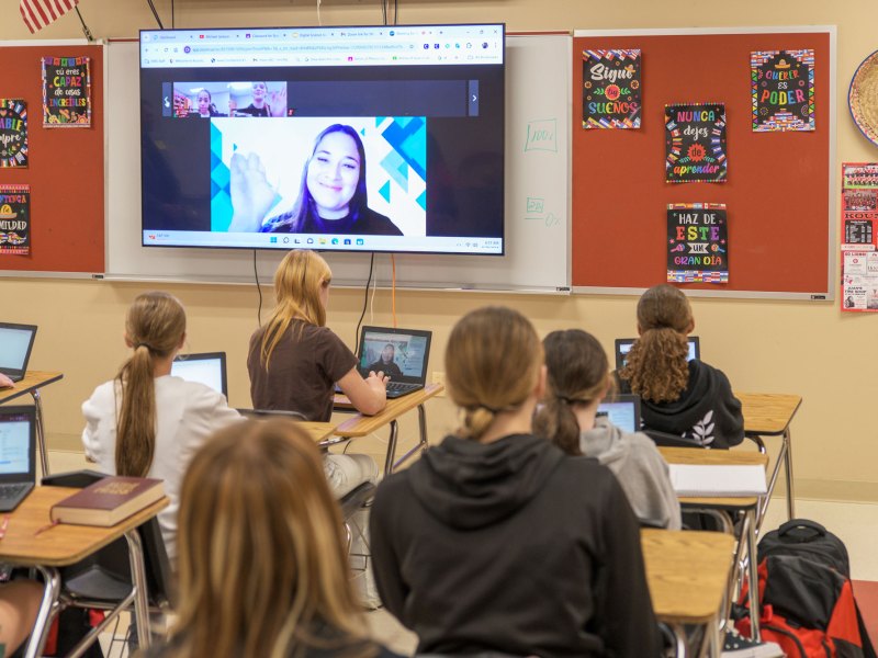Students learning with a virtual teacher projected in the front of the classroom