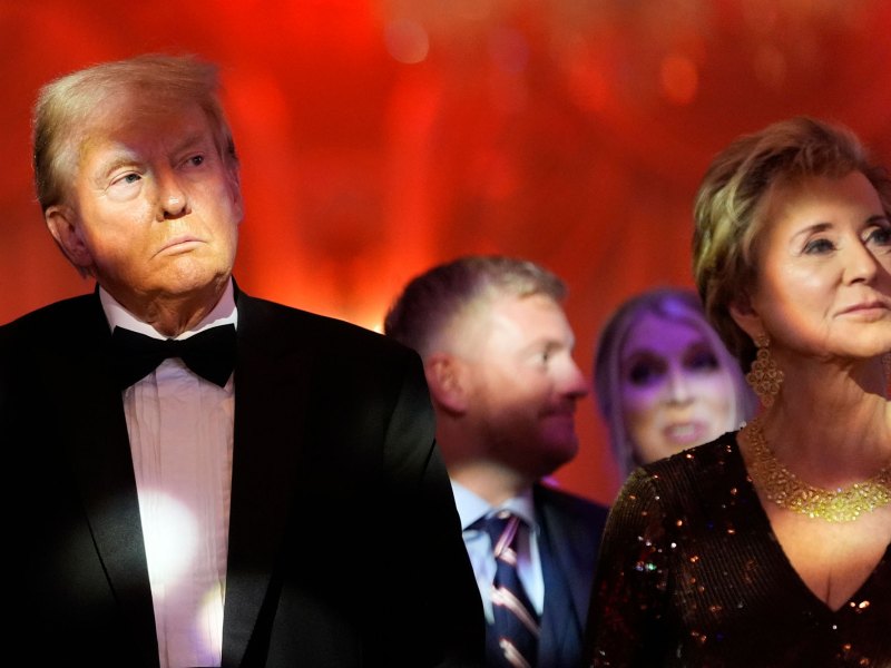 A Man and women wearing formal black clothes stand next to each other in front of an orange background.
