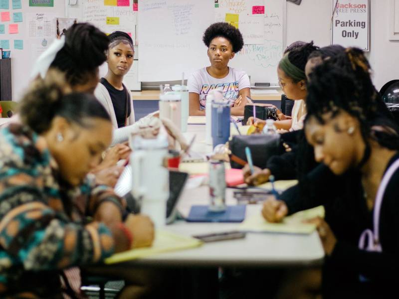 Students sit around a table, writing