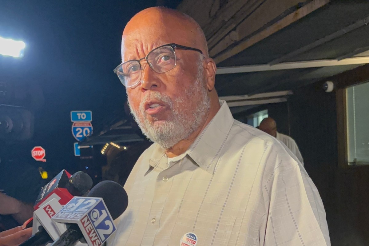 A bearded man wearing glasses speaks into reporter microphones outside at night