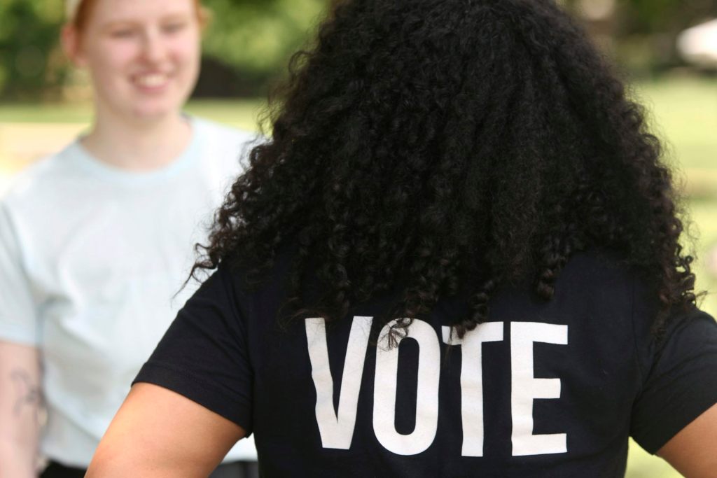 woman faces away from camera, wearing a 'VOTE' t shirt