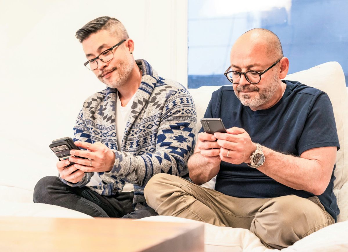 Two men sit on a couch and look at their cell phones