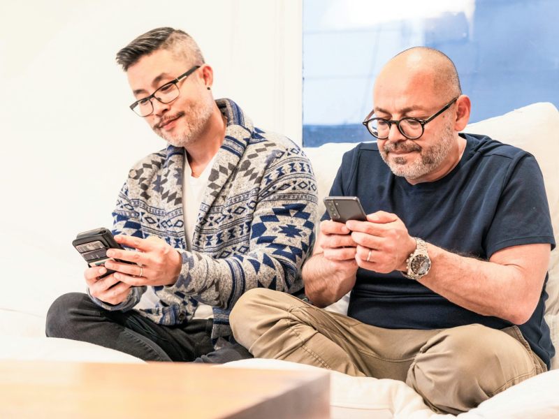 Two men sit on a couch and look at their cell phones