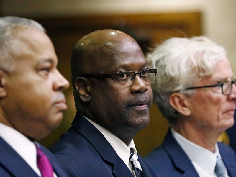Three men in blue suits sit in a line in a courtroom