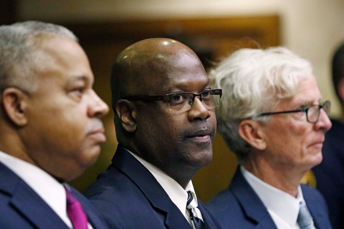 Three men in blue suits sit in a line in a courtroom