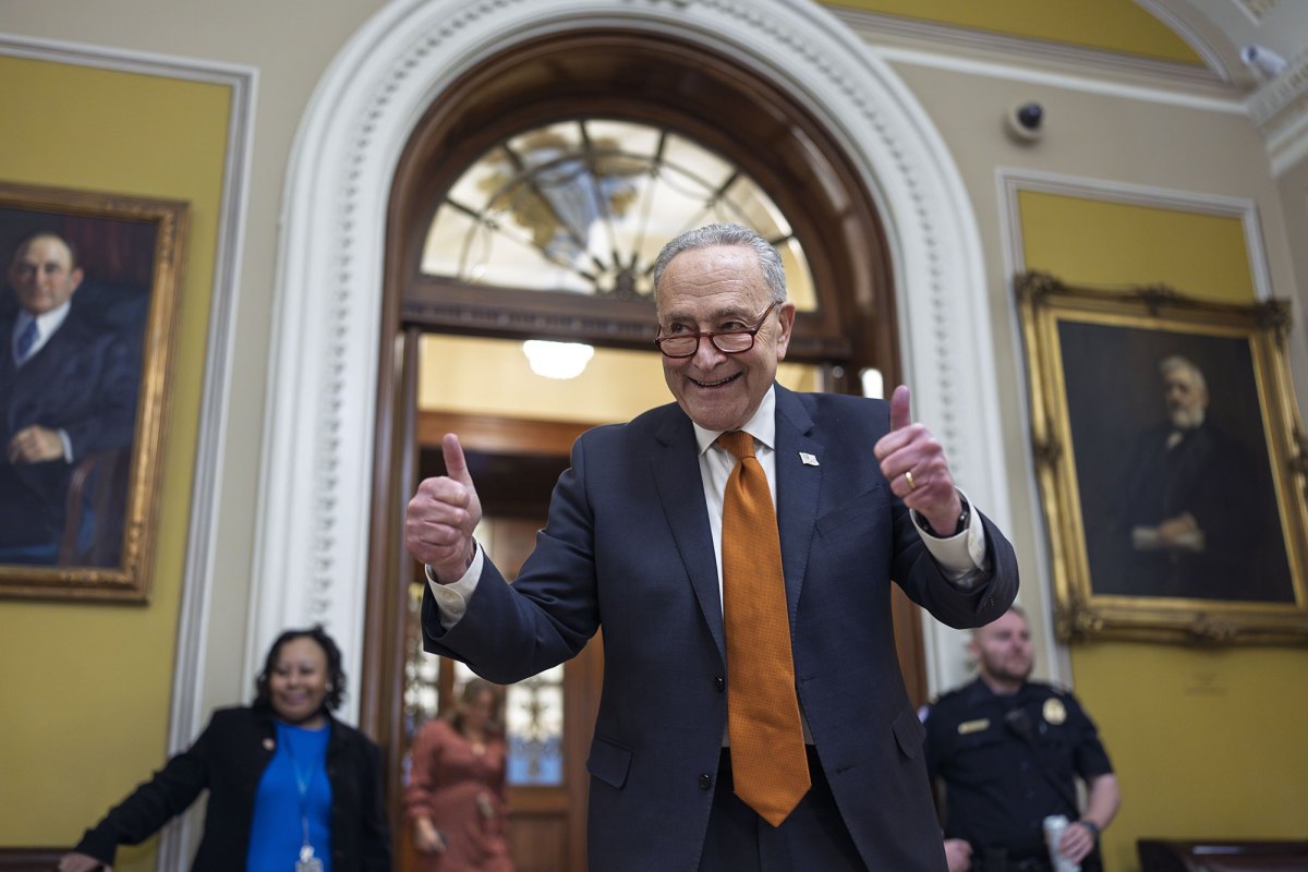 A older man in a suit and brown tie does a smiling pose with two thumbs up