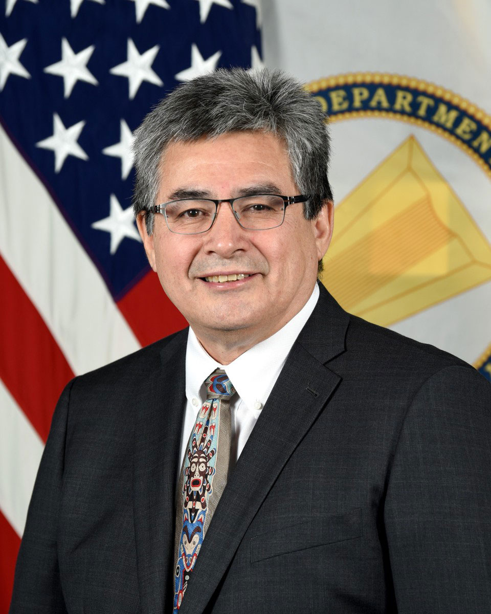a man in a suit and tie poses in front of the US flag