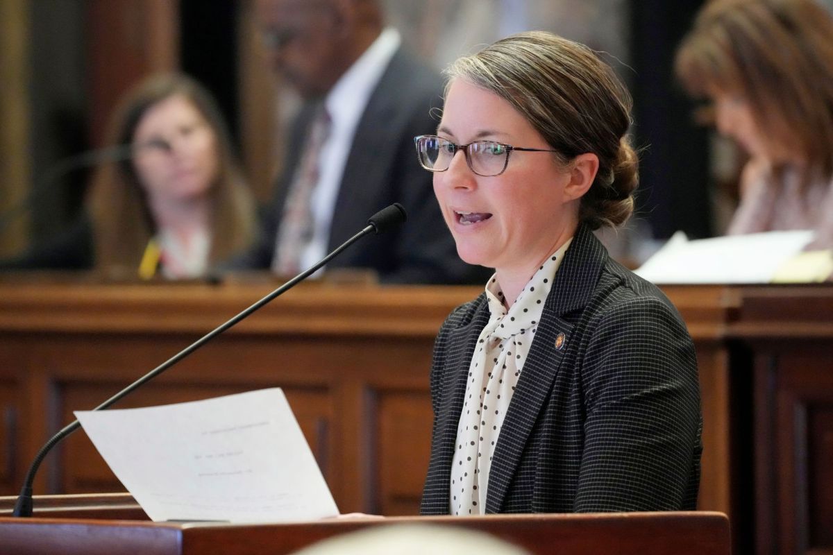 A woman in glasses speaks at a podium with a paper in her hand
