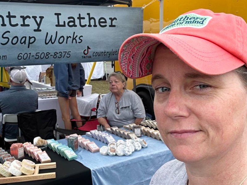 A white woman standing before a market booth selling soaps