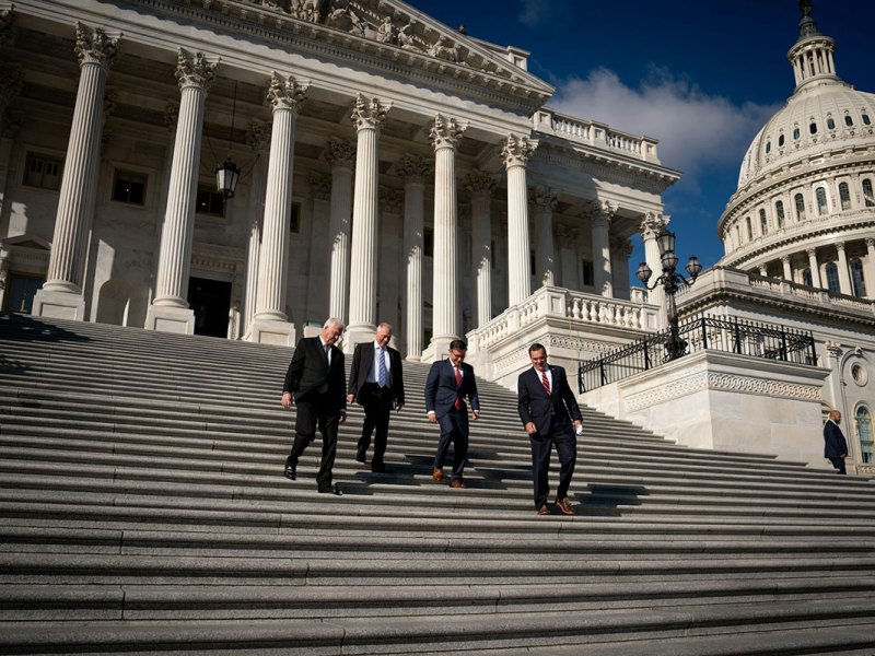Four men in dark suits walk down the steps of the US Capitol