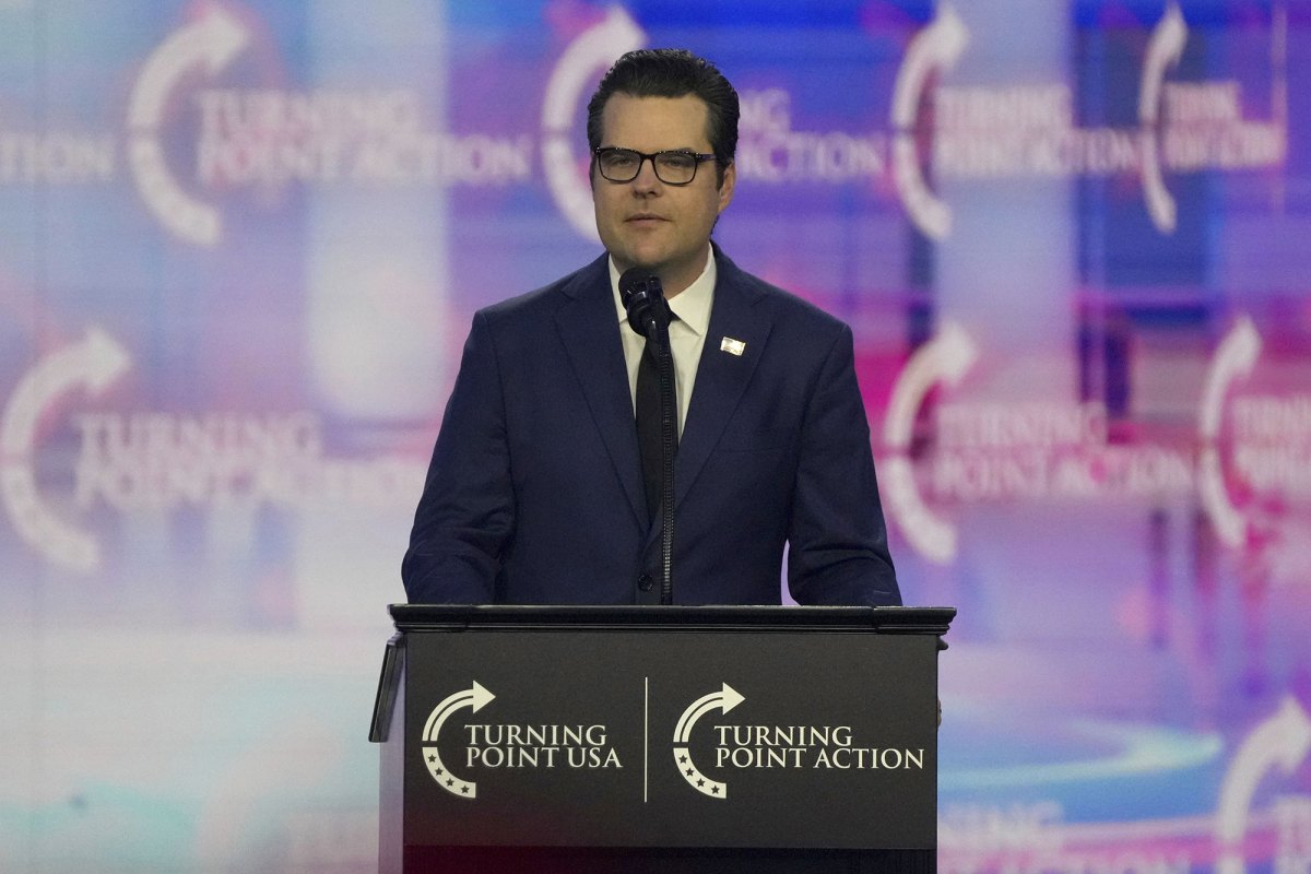 A man in a navy suit stands behind a podium on a stage. The logo for Turning Point USA is repeated everywhere.