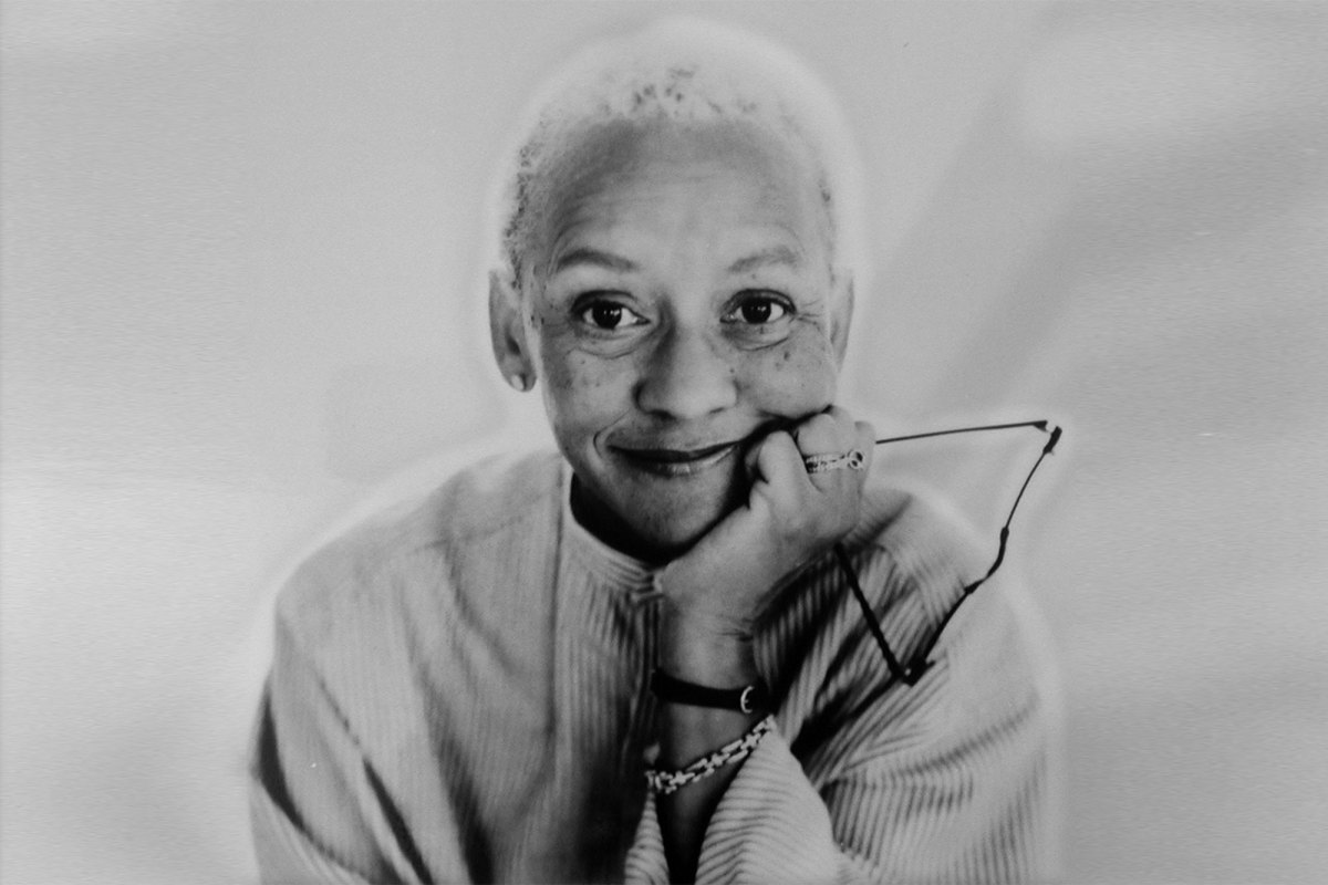 Black and white portrait of a woman with short hair, smiling and holding her glasses in one hand
