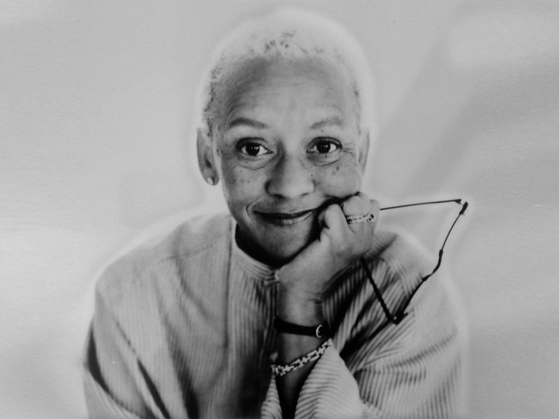 Black and white portrait of a woman with short hair, smiling and holding her glasses in one hand