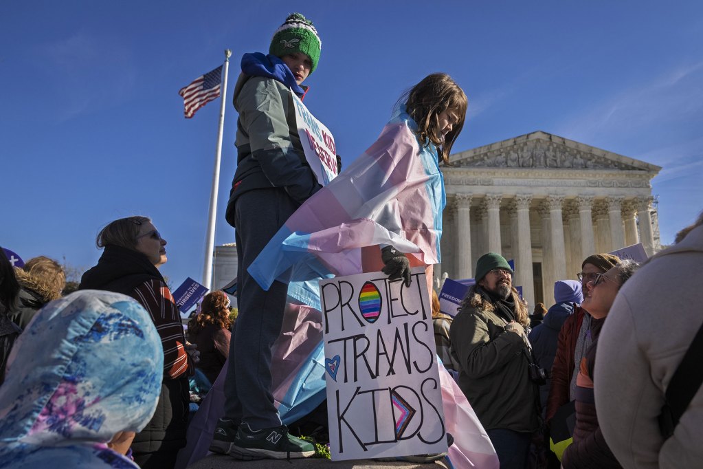Kids hold hold signs and transgender pride flags outside of the supreme court