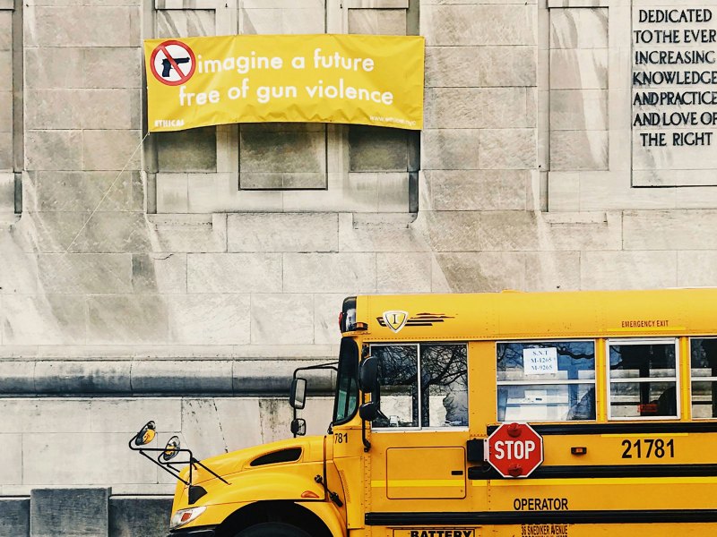 A yellow school bus sits outside of a building with a yellow banner that reads "Imagine a future free of gun violence"