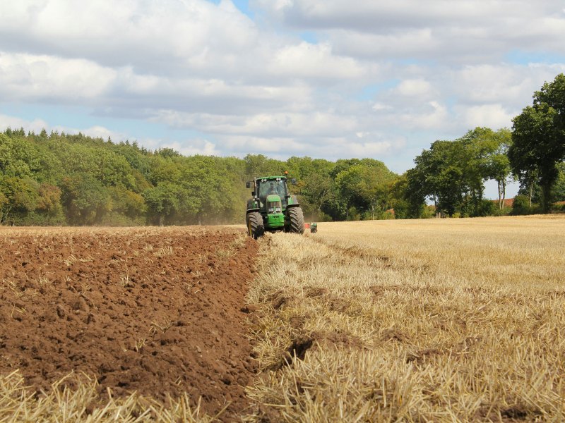 A green tractor tills a field and exposes fresh dirt