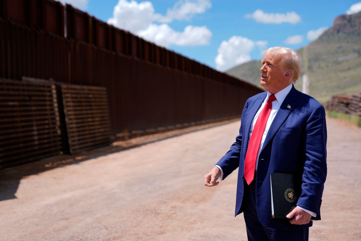 A older man in a blue suit and red tie looks up at a tall metal wall