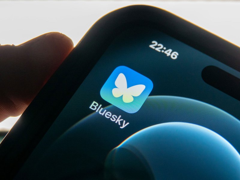 A picture of a phone in someone's hand, with an app icon for Bluesky visible