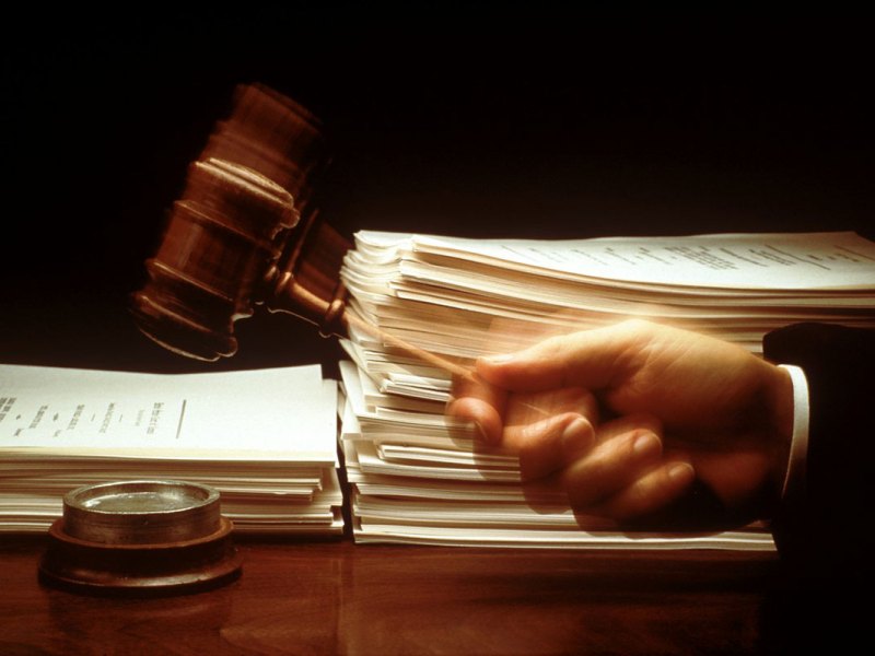 A judge's hand hits a gavel before piles of paperwork