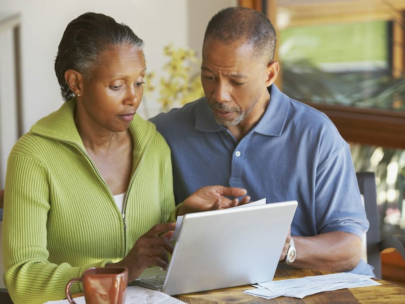 Two older people look through a laptop and papers together