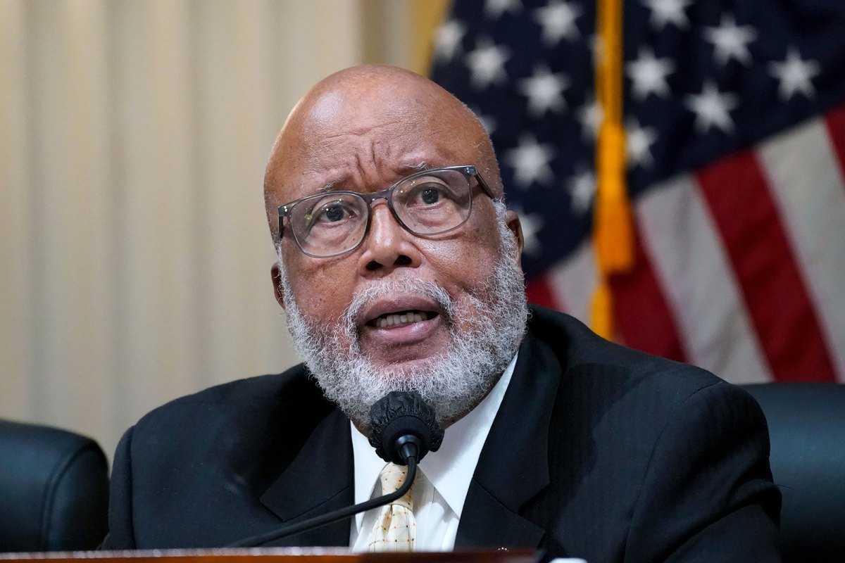 A man speaks at a mic. The US Flag can be seen behind him