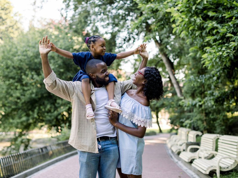 Young happy laughing black couple spending time together in an park, a young daughter riding on the father's shoulders