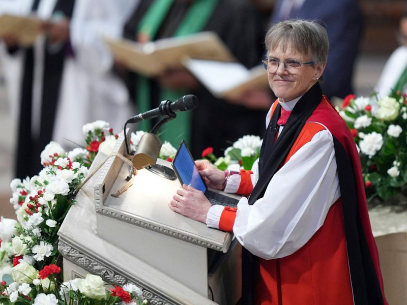 A woman in red and white Bishop robes stands at a church podium