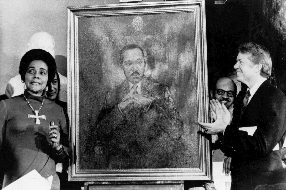 A black woman and a white man stand beside a painted portrait of Martin Luther King, Jr. and clap