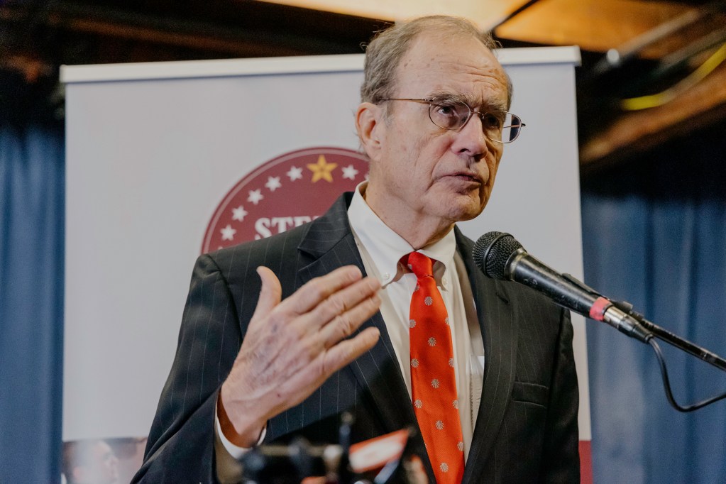 Politician with red tie speaking at a press conference.