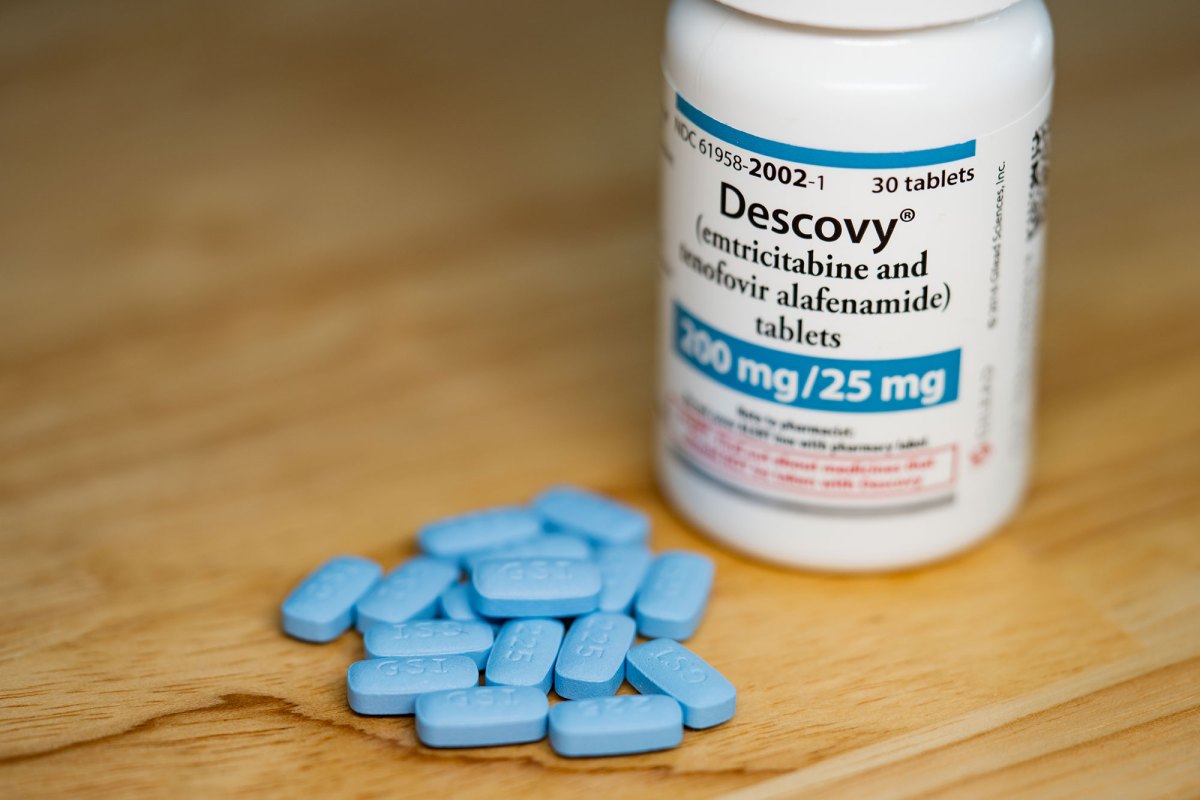 A white pill bottle labeled Descovy sits beside a pile of blue pills