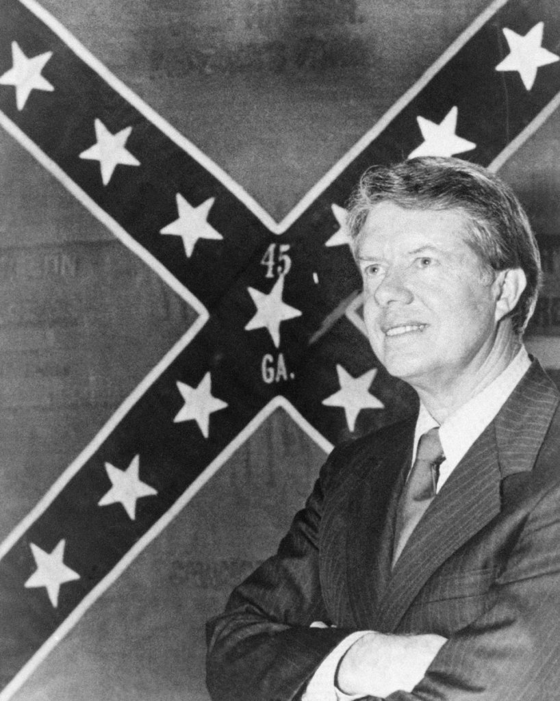 An old black and white photo of a man in a suit posed in front of a confederate flag that says 45 GA in the center