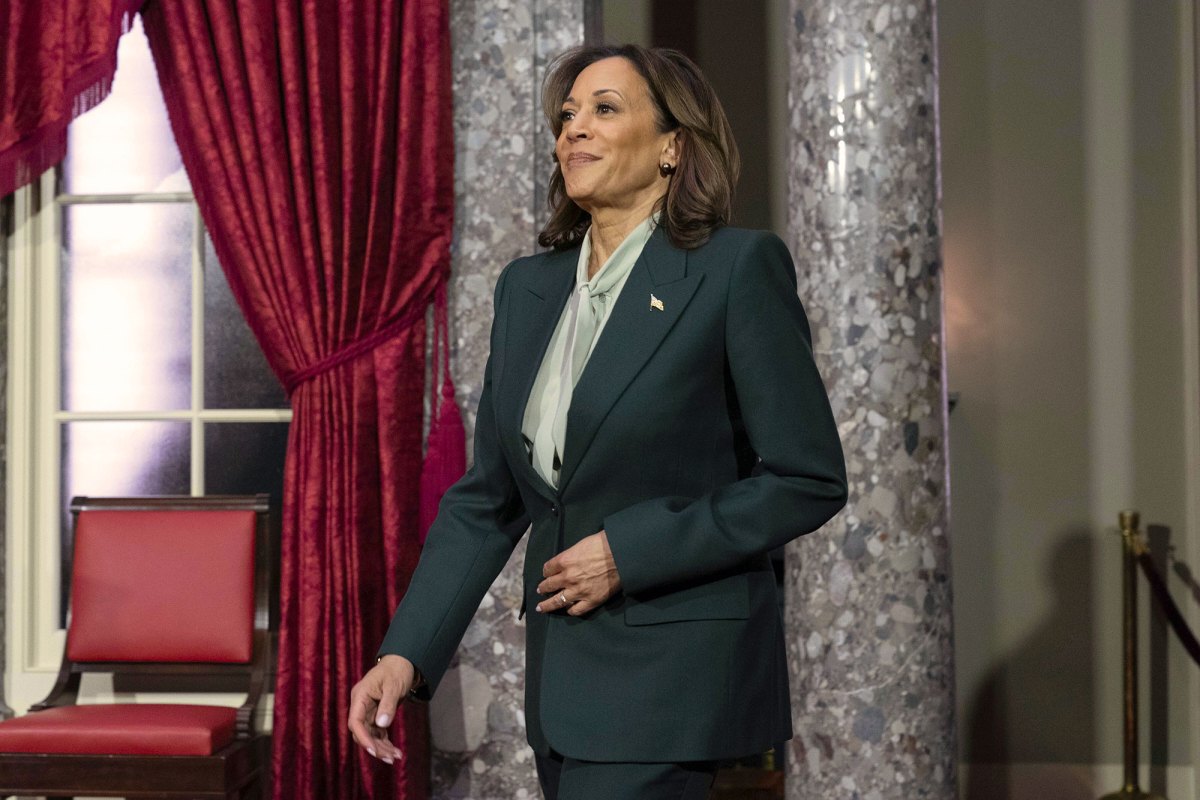 A woman in a suit walks into a room with marble columns and red velvet curtains