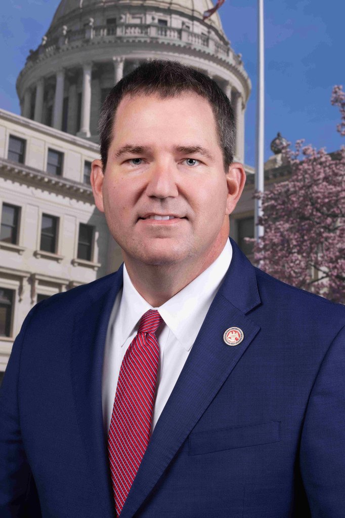 Official portrait of a man in a blue suit posed in front of the capitol building