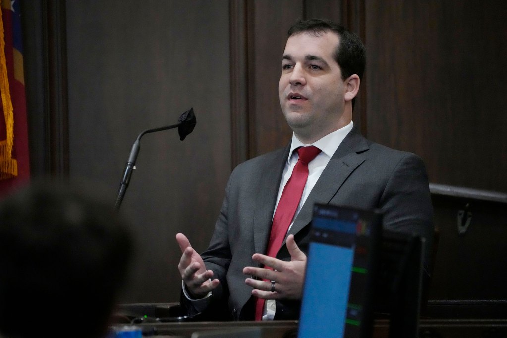 A man in a suit speaks at a mic during a legislative meeting
