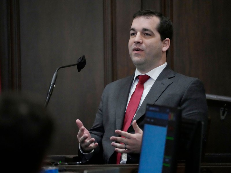 A man in a suit speaks at a mic during a legislative meeting