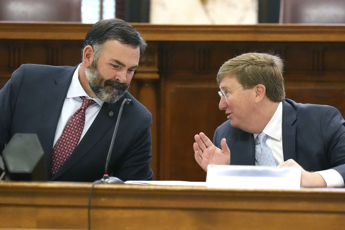 Two men in suits lean in behind a desk and talk
