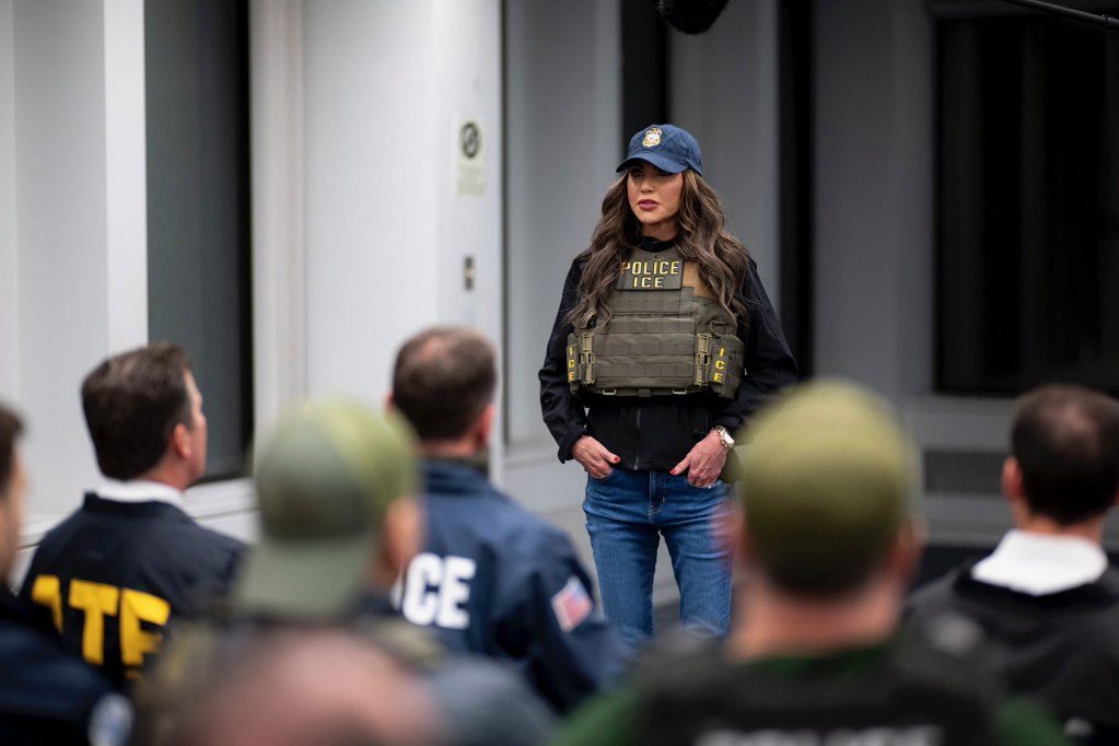 A woman in a vest that says POLICE ICE speaks to a room of seated police