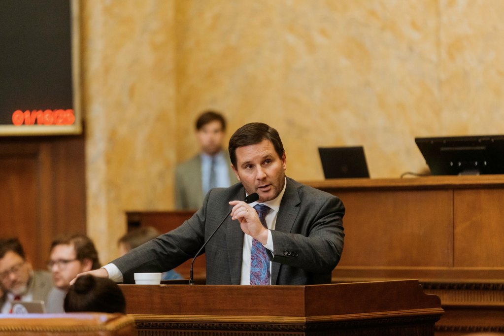 A man in a suit speaks into a mic at a podium