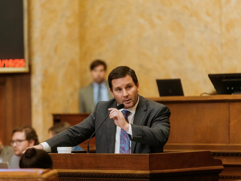 A man in a suit speaks into a mic at a podium