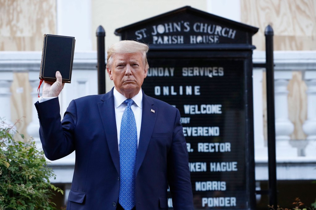 A man holds a bible in the air in front of a sign for St John's Church