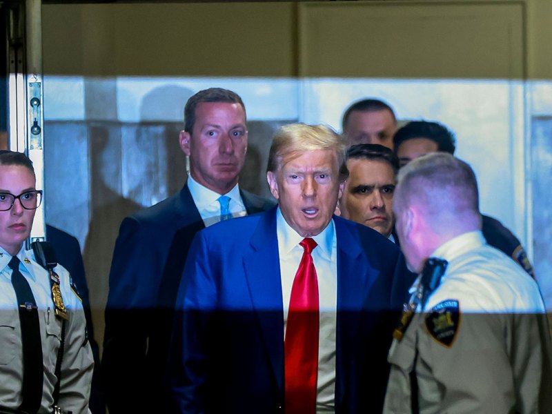 Former President Donald Trump arrives for the start of a court hearing, surrounded by security.