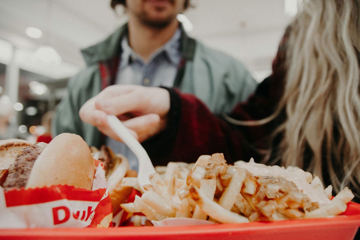 A closeup of a woman eating fast food french fries from a red tray