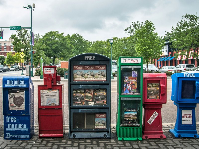 A row of colorful newspaper boxes on the sidewalk
